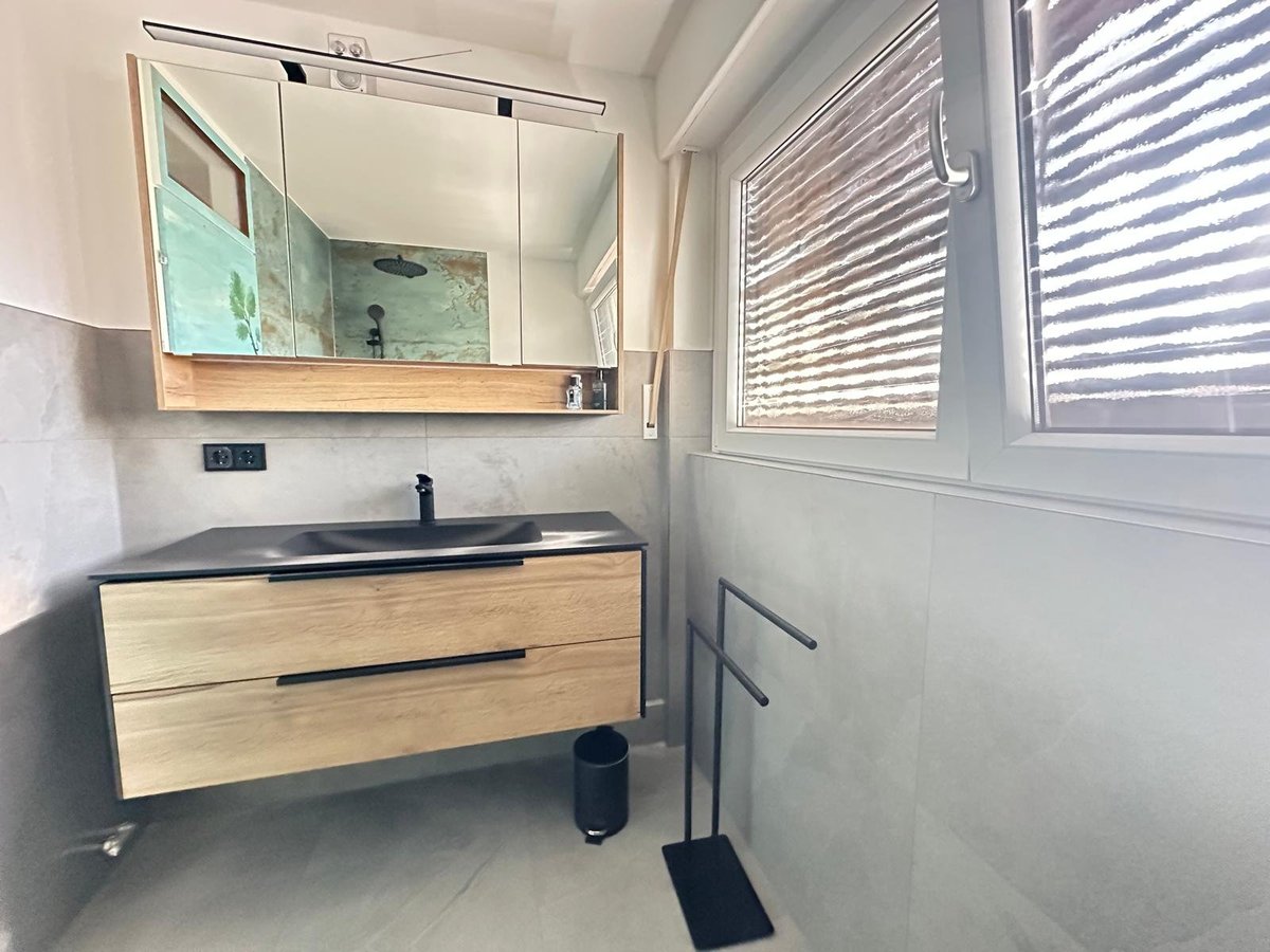 Modern bathroom with light wood vanity, vessel sink, large mirror, and window with blinds