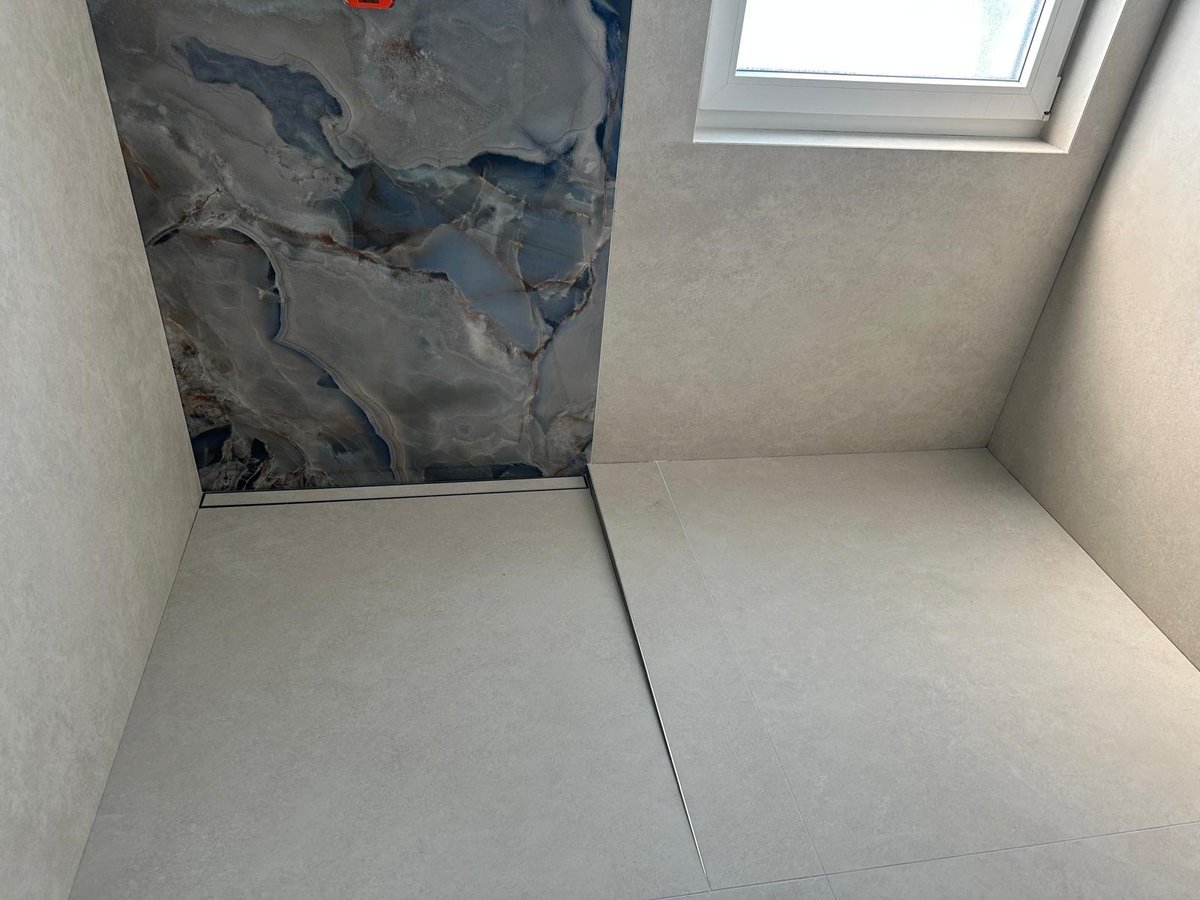 Unfinished bathroom corner with gray drywall, concrete floor, and small skylight window above dark water-damaged patch on wall