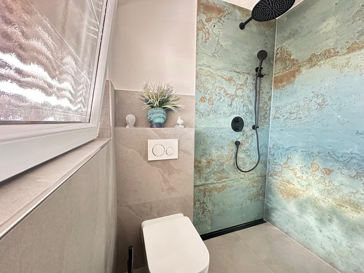 Modern bathroom with wall-mounted toilet, beige tile wall, potted plant, and glass shower enclosure with turquoise distressed tile