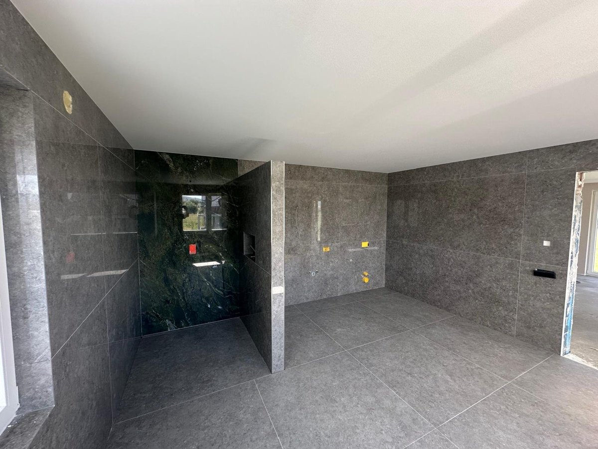 Modern bathroom under construction with dark tile walls, white ceiling, and concrete flooring