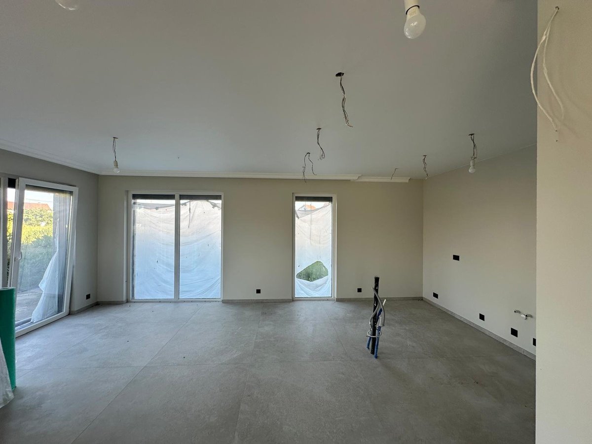 Empty room under construction with concrete floor, large windows, and visible electrical wiring in ceiling