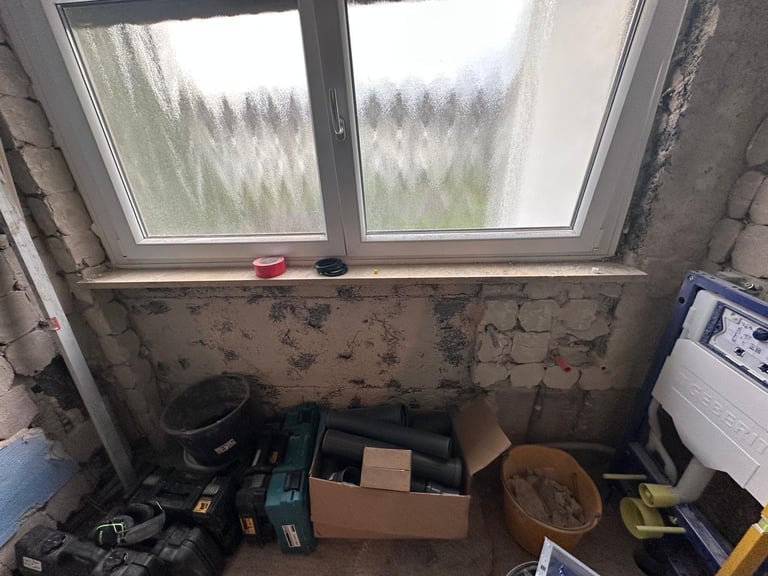 Cluttered room interior with large windows overlooking forest, boxes and tools scattered on floor, deteriorating walls