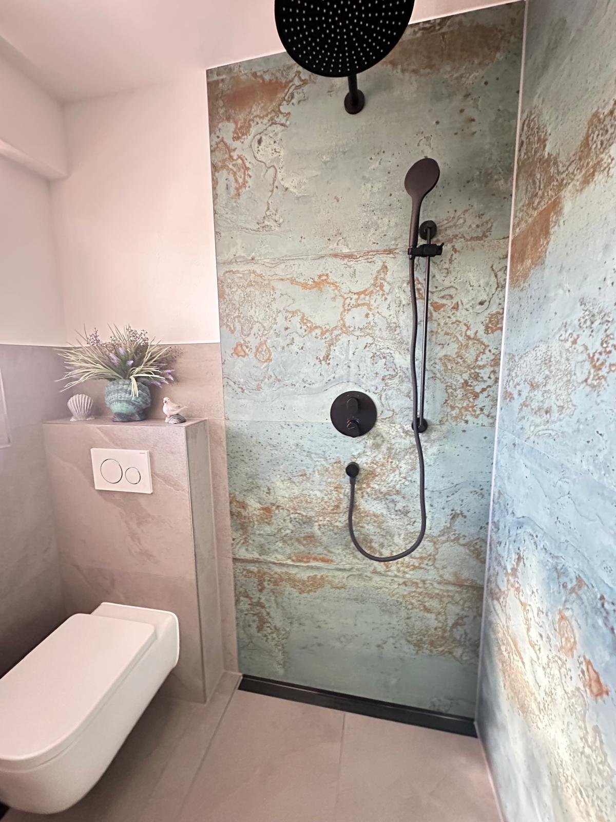 Modern bathroom with walk-in shower featuring weathered marble-effect tiles, black rainfall showerhead, and handheld sprayer