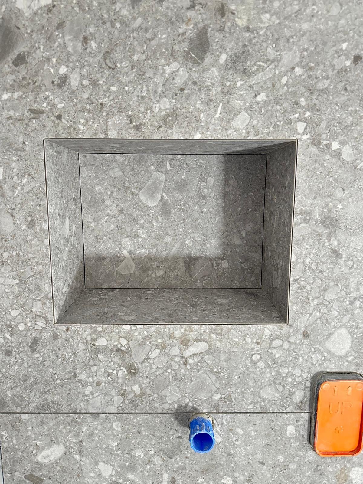 Empty concrete niche or recessed box in gray textured wall with blue object and orange item below it