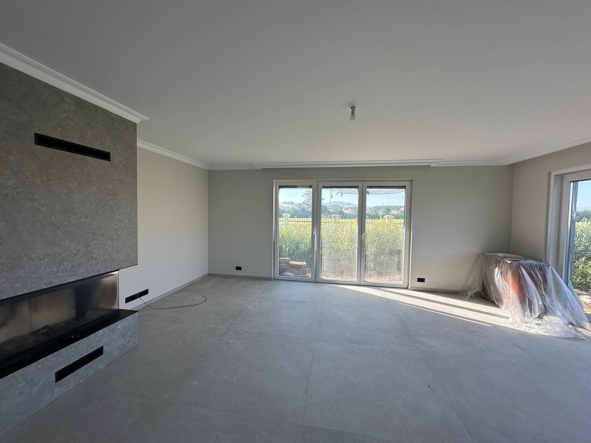 Empty modern living room with large windows, polished concrete flooring, and minimalist decor overlooking landscape