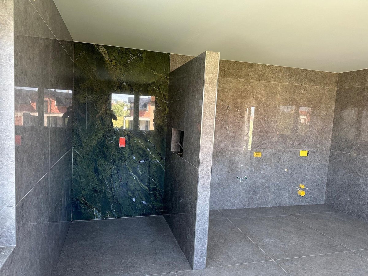 Interior of concrete structure with dark tiled walls, glass panels, and yellow utility markers on unfinished surfaces